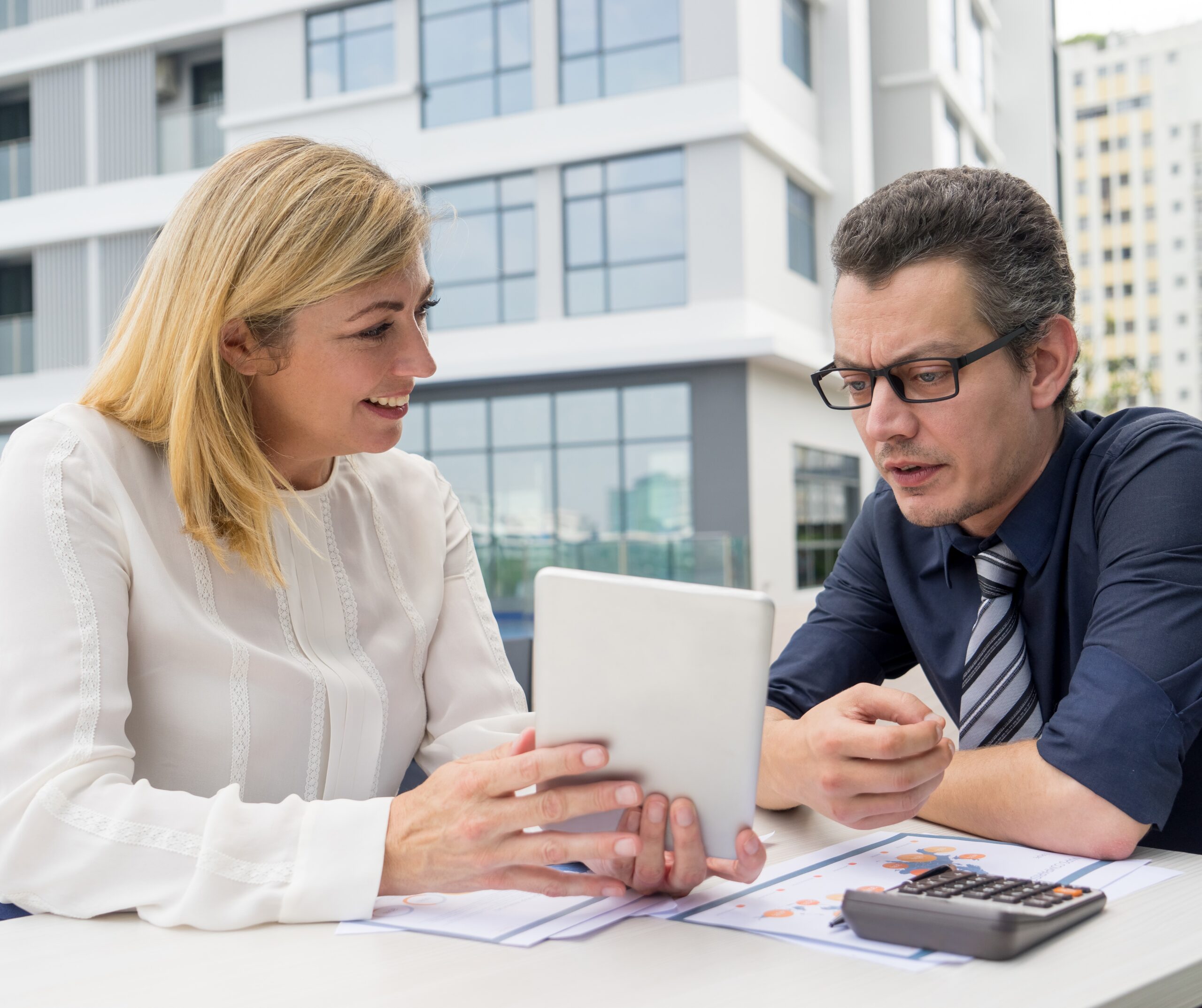 About Us 2 smiling woman showing male colleague tablet screen cafe outdoors scaled